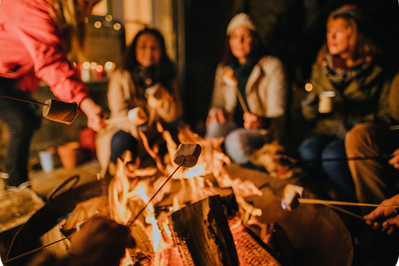 Viele Personen sitzen um eine Feuerschale und rösten Marshmallows