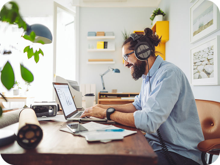 Mann sitzt mit einem Headset auf dem Kopf vor einem Laptop