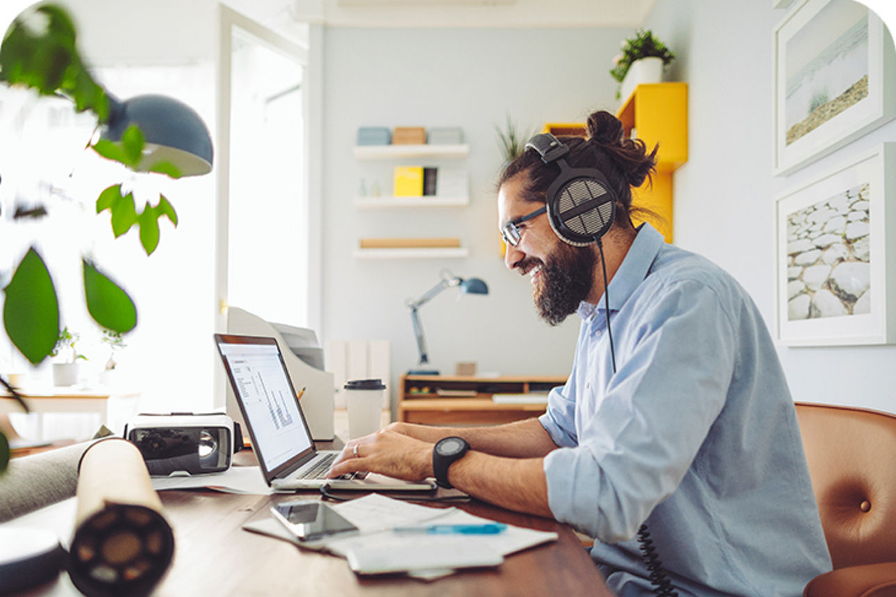 Mann sitzt mit einem Headset auf dem Kopf vor einem Laptop