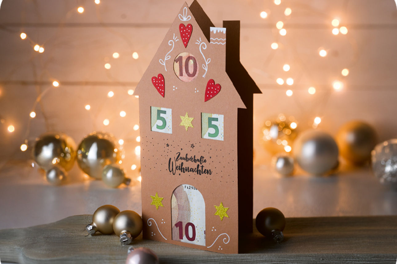 Lebkuchenhaus-Geldgeschenk umgeben von Weihnachtsdekoration
