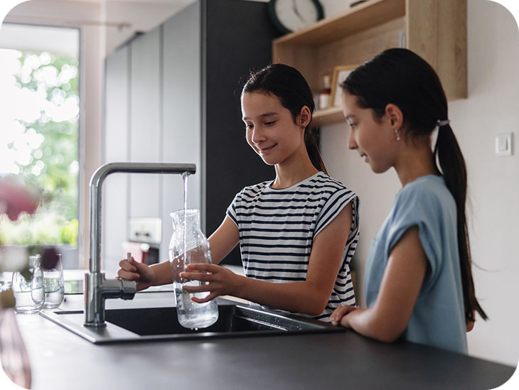 Zwei Kinder füllen eine Flasche am Wasserhahn in der Küche