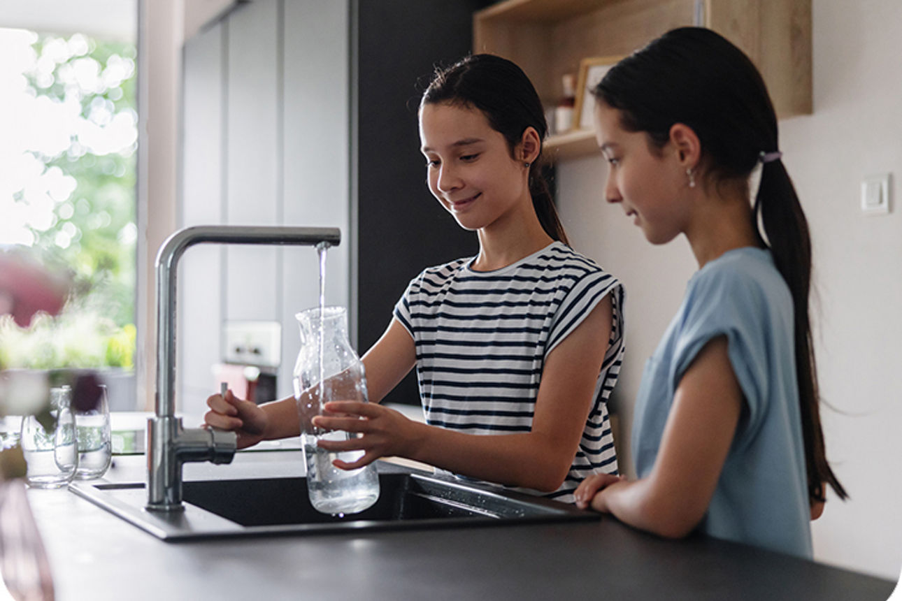 Zwei Kinder füllen eine Flasche am Wasserhahn in der Küche
