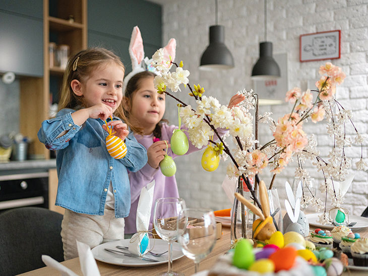 Zwei Kinder schmücken Äste in einer Vase mit Ostereiern