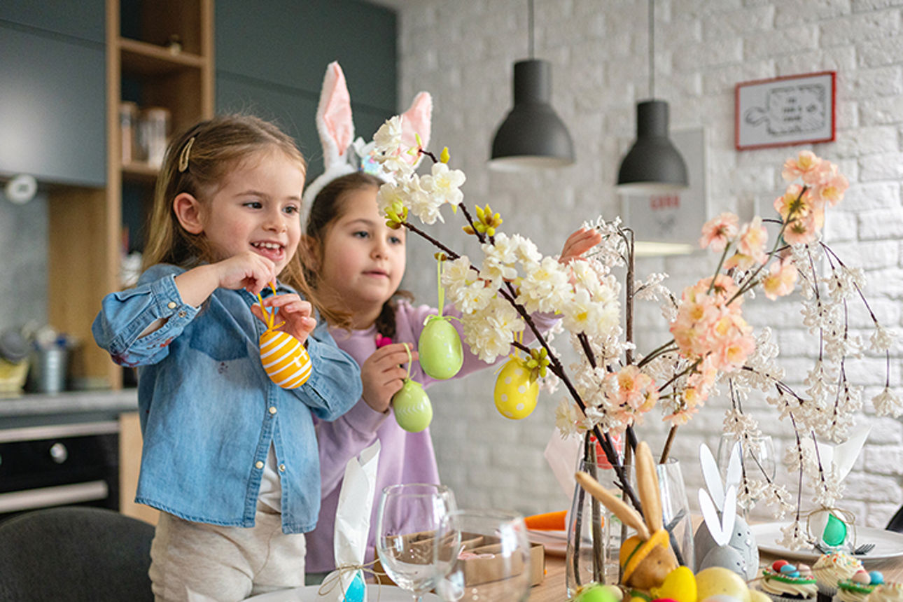 Zwei Kinder schmücken Äste in einer Vase mit Ostereiern