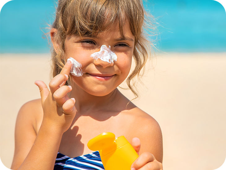 Kind am Strand streicht sich Sonnencreme ins Gesicht