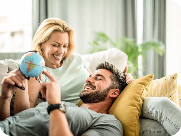 Paar liegt auf dem Sofa und hält einen kleinen Globus in der Hand