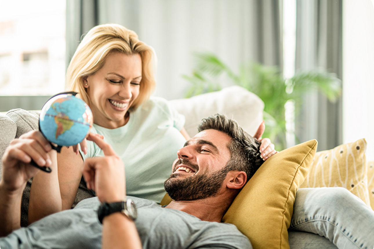 Paar liegt auf dem Sofa und hält einen kleinen Globus in der Hand