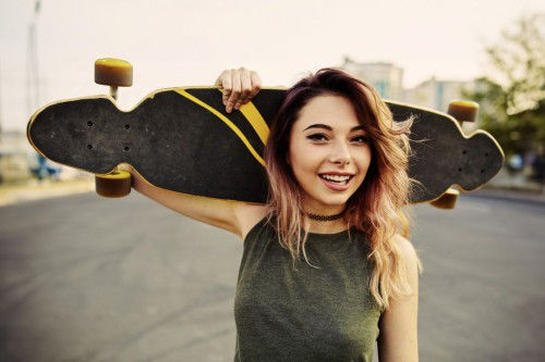 Junges Mädchen in einem Skatepark mit einem Skateboard auf der Schulter.