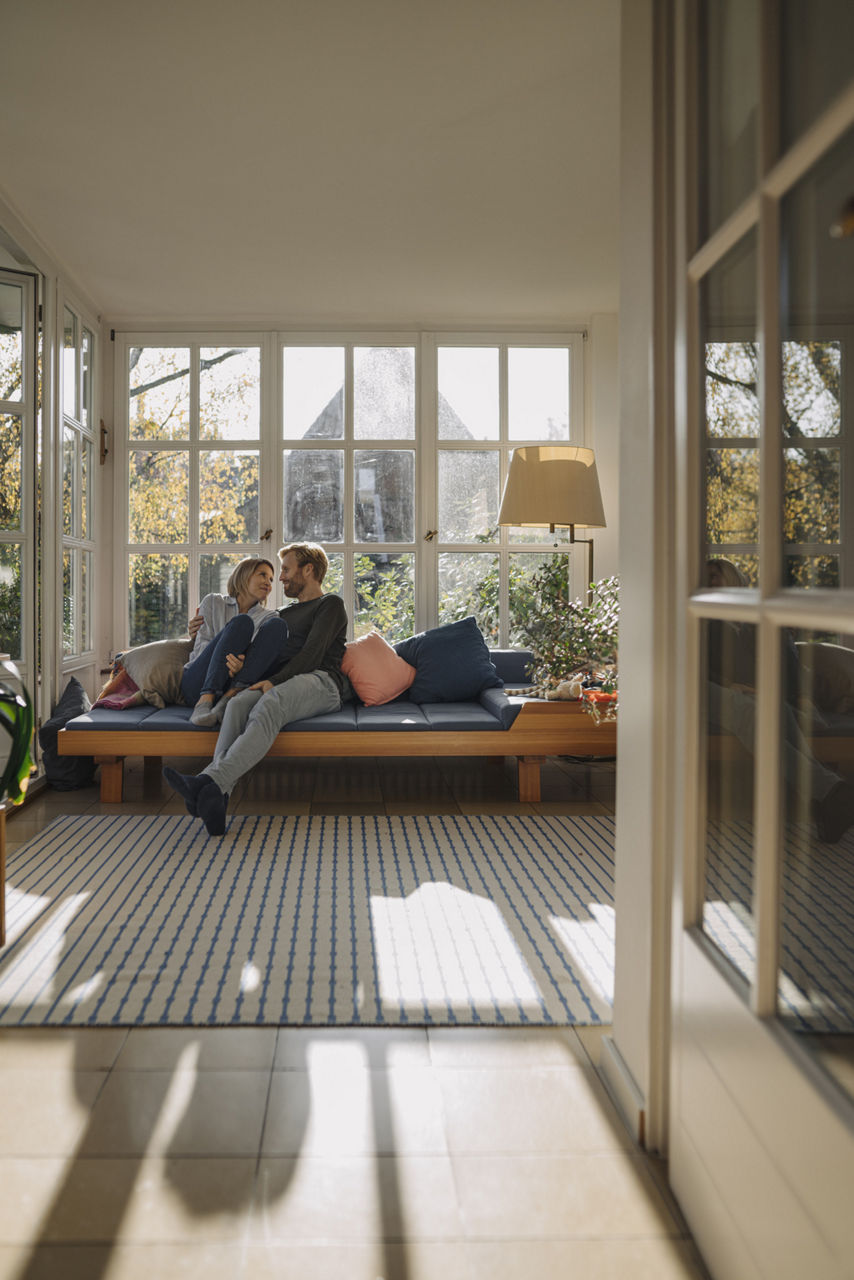 Ehepaar sitzt im sonnendurchfluteten Wohnzimmer auf einem Sofa