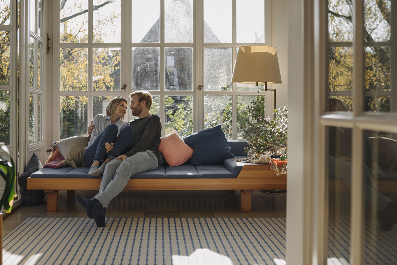 Ehepaar sitzt im sonnendurchfluteten Wohnzimmer auf einem Sofa
