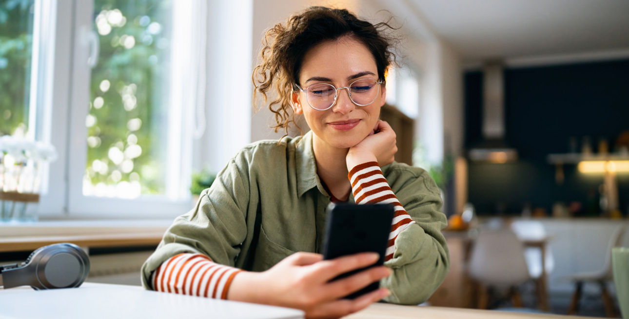 Junge Frau sitzt am Schreibtisch und schaut auf ihr Smartphone