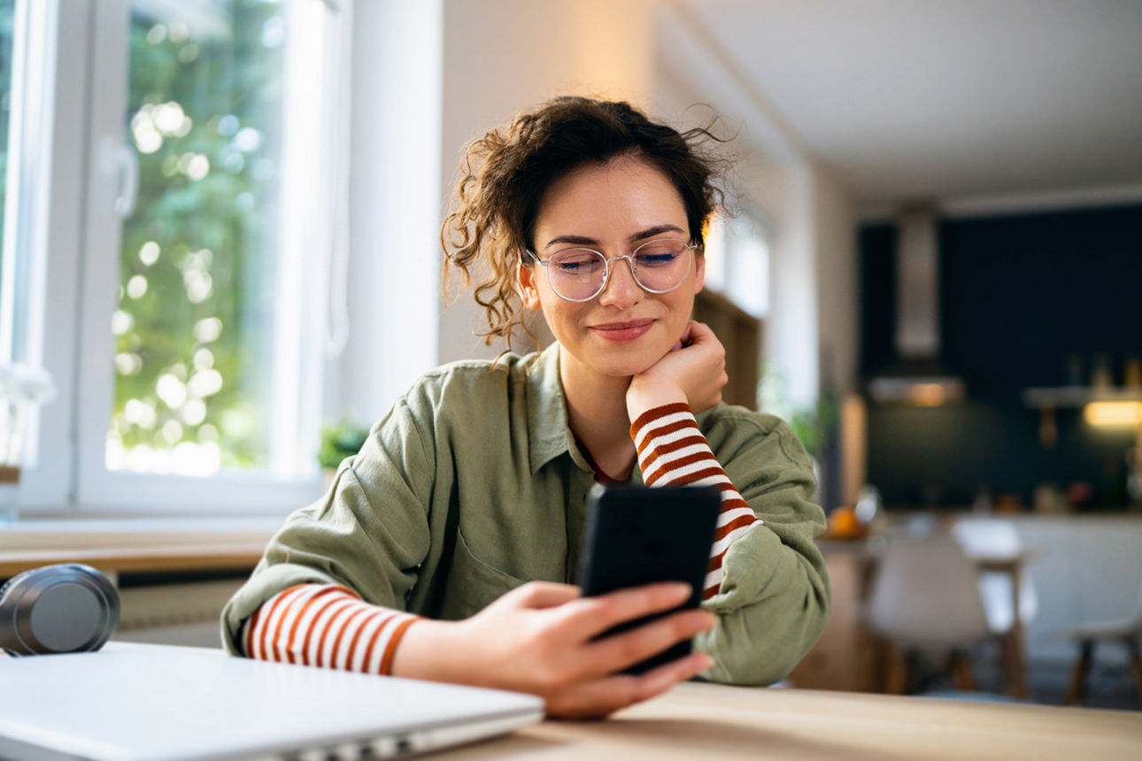 Junge Frau sitzt am Schreibtisch und schaut auf ihr Smartphone