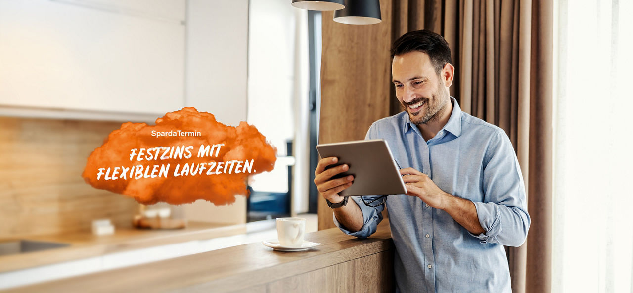 Junger Mann steht mit Tablet in der Hand in einer Küche und schaut mit einem Lachen im Gesicht auf ein Tablet, welches er in der Hand hält. Links im Bild steht auf einer orangenen Fläche "SpardaTermin: Festzins mit flexiblen Laufzeiten."