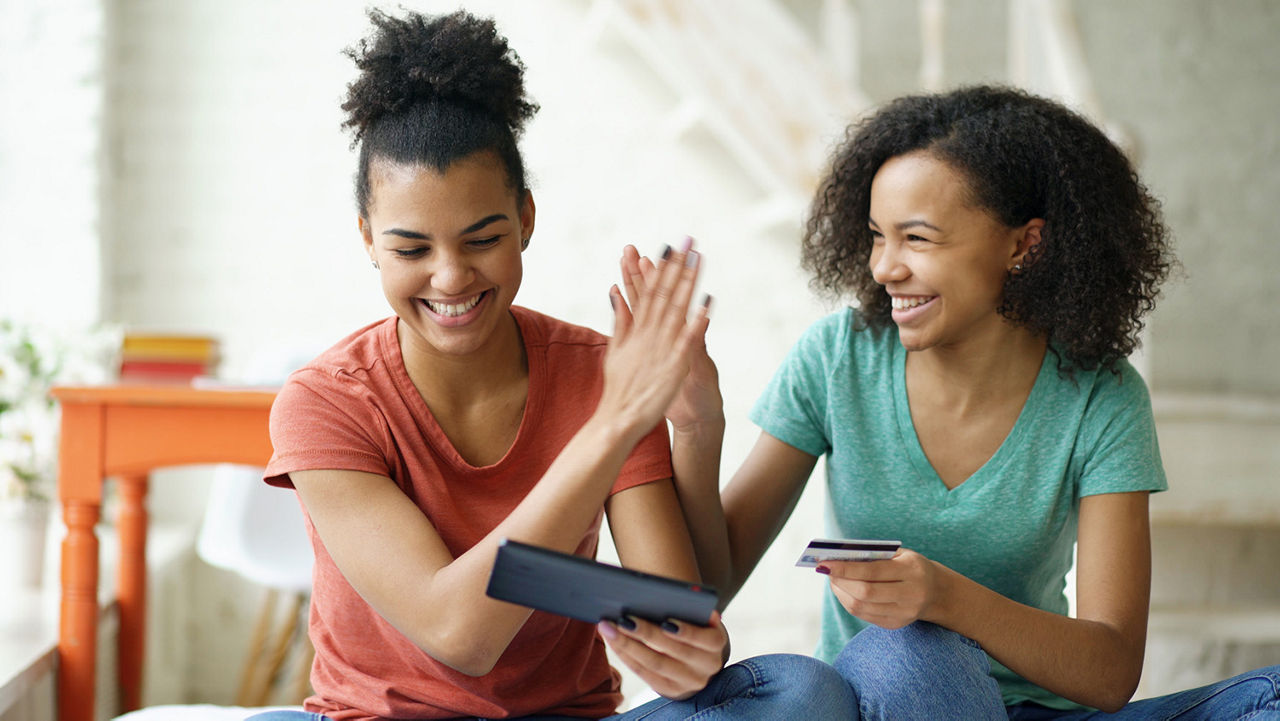 Zwei Frauen die lächelnd nebeneinander sitzen, ihre Smartphones in der Hand halten und sich abklatschen