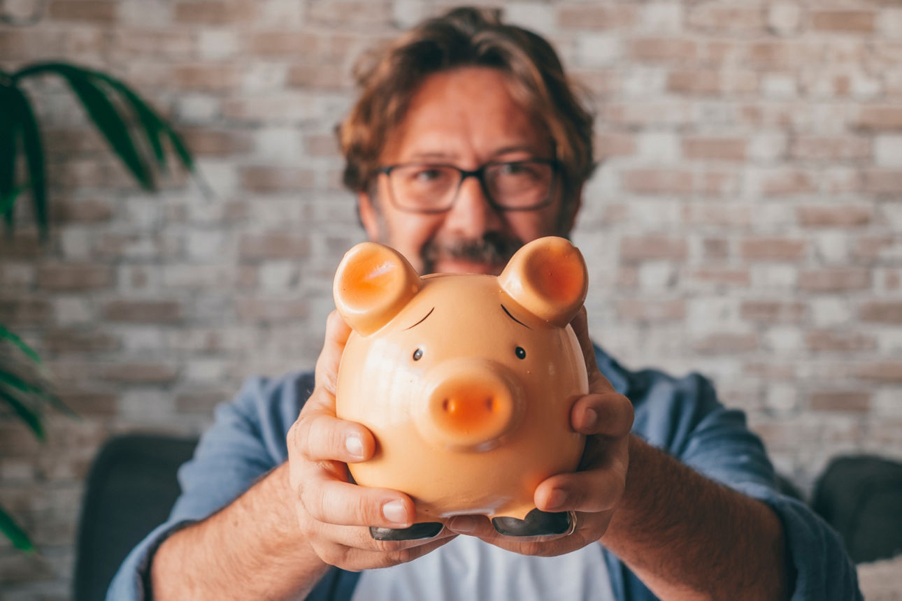 Mann hält ein oranges Sparschwein in den Händen