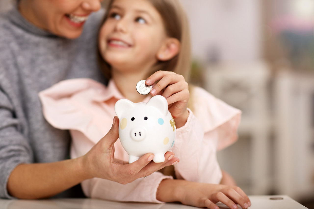 Picture of young girl and her mother with piggybank sitting at table