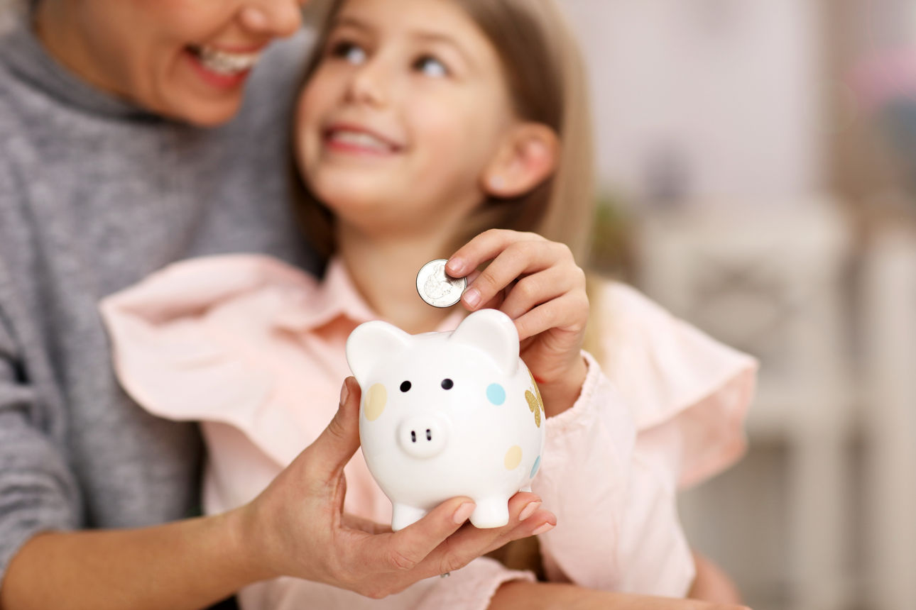 Picture of young girl and her mother with piggybank sitting at table