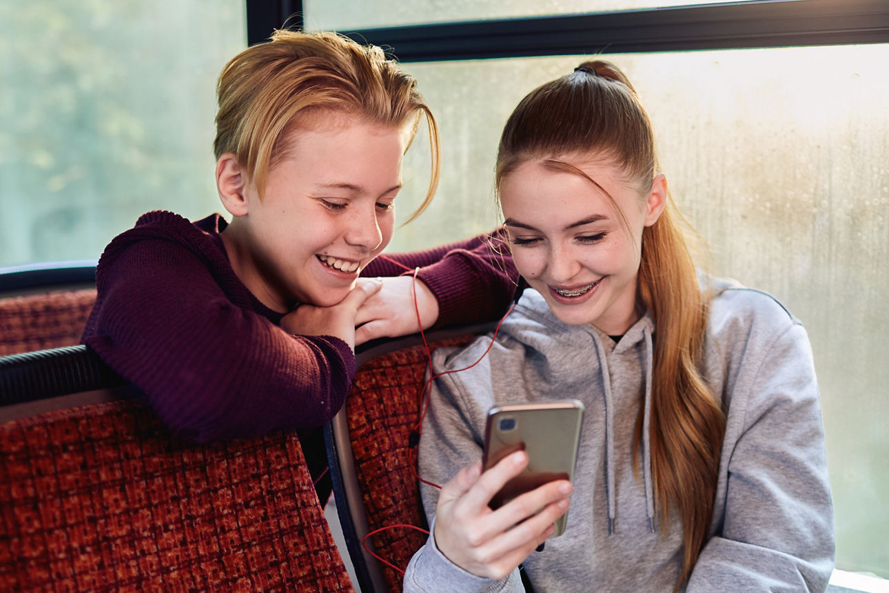Zwei Jugendliche lachend im Bus schauen auf ein Handy