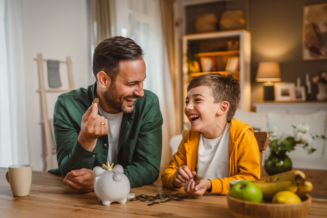 Vater und Sohn sparen gemeinsam Geldmünzen am Sparschwein zu Hause