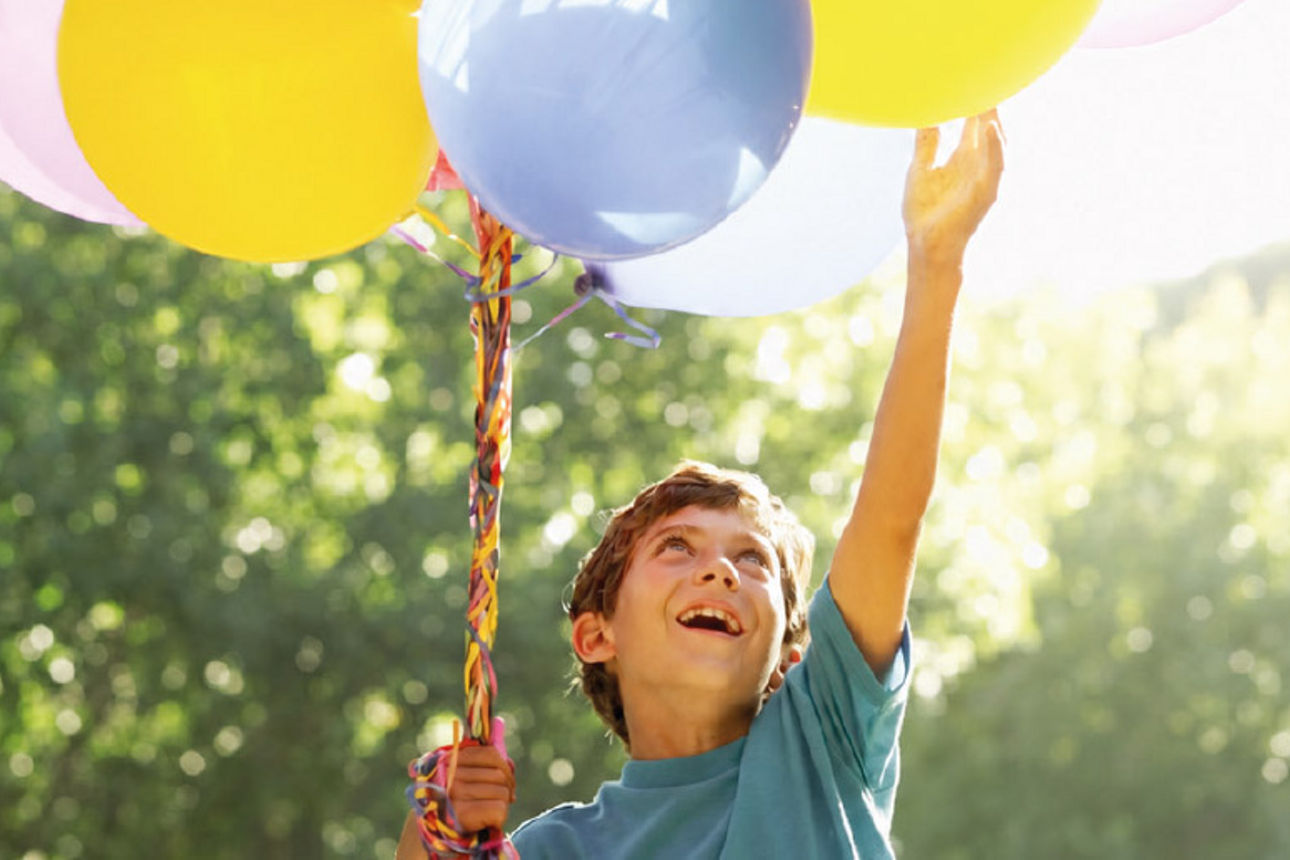 Ein fröhliches Kind hält ein Bündel Luftballons in der Hand