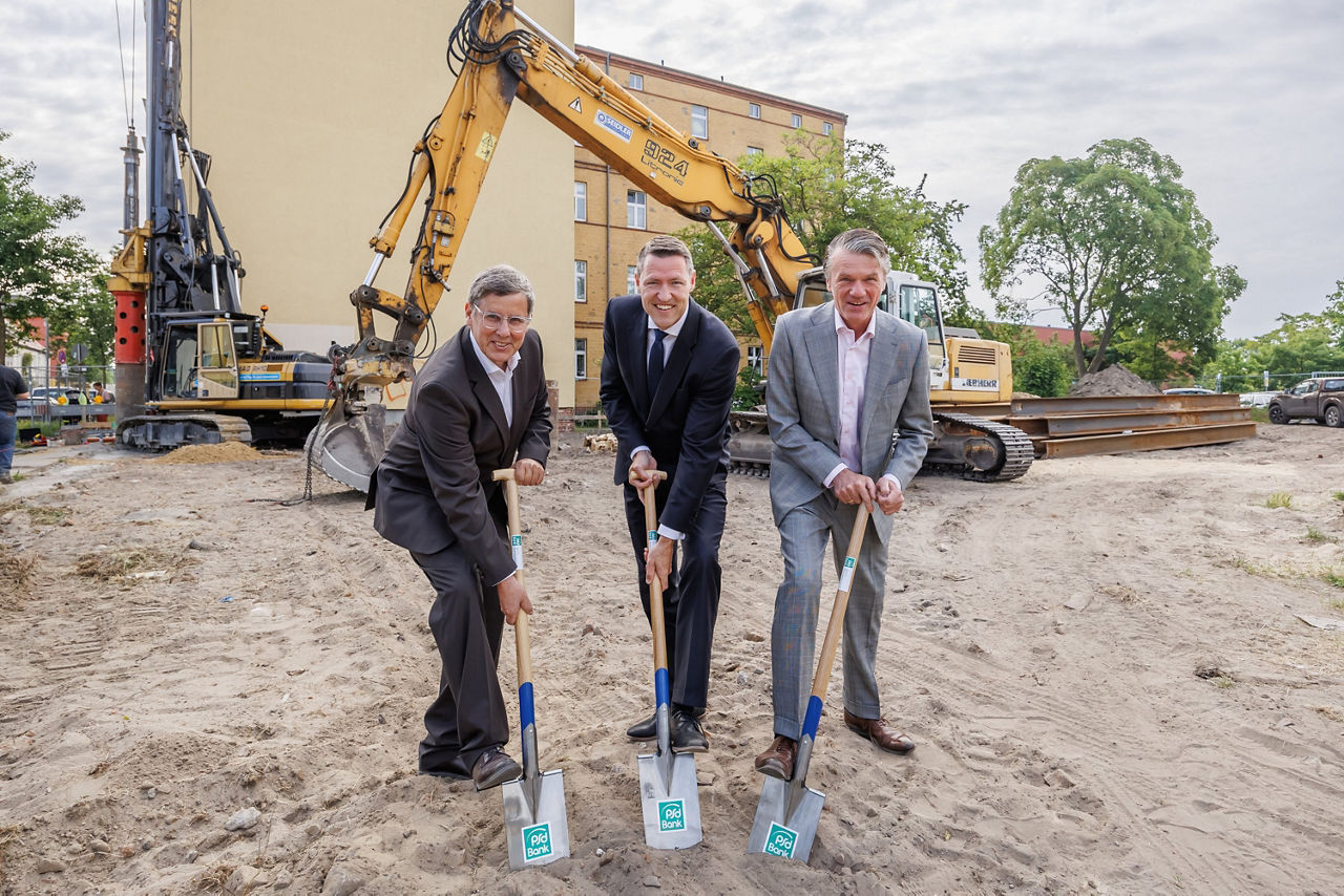 PSD Vorstand und zwei Architekten lächeln beim Spatenstich für einen Neubau in die Kamera