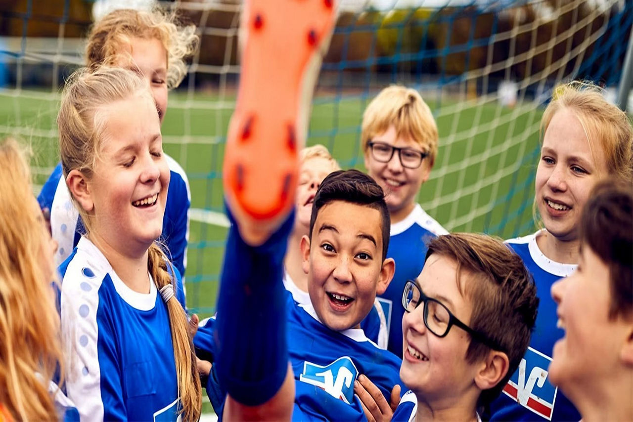 Gruppe von Kindern mit blauen Trikos während einer aus der Gruppe seine Fußsole zeigt die orange ist. 