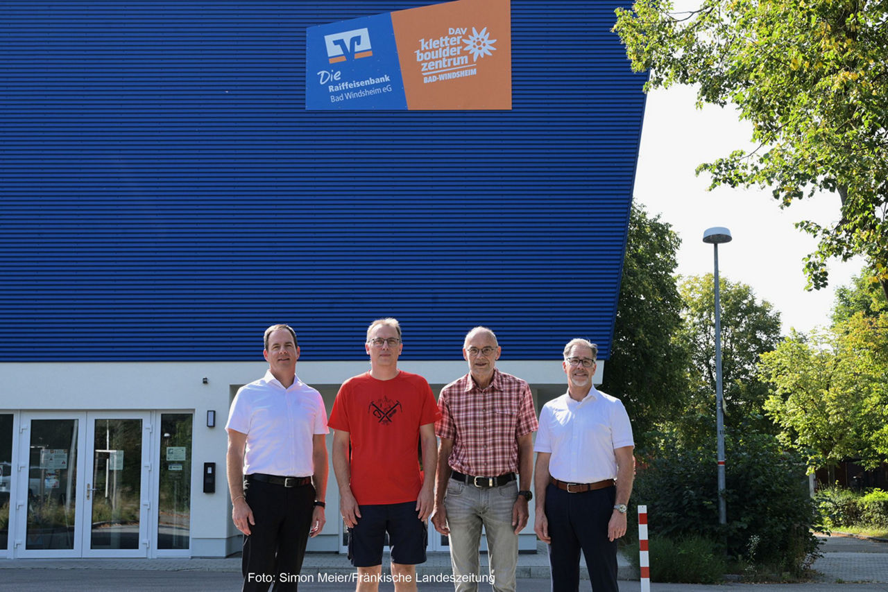 Vier  Männer (links und rechts mit weißem Hemd und schwarzer Hose und in der Mitte mit rotem T-Shirt und kurzer dunklen Hose,
