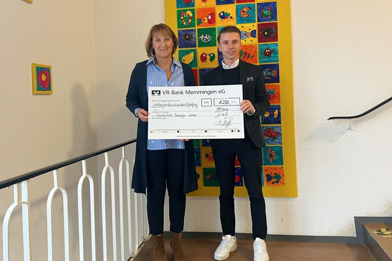 Rektorin der Schule steht neben Geschäftsstellenleiter Tim Glogger mit symbolischen Spendenscheck