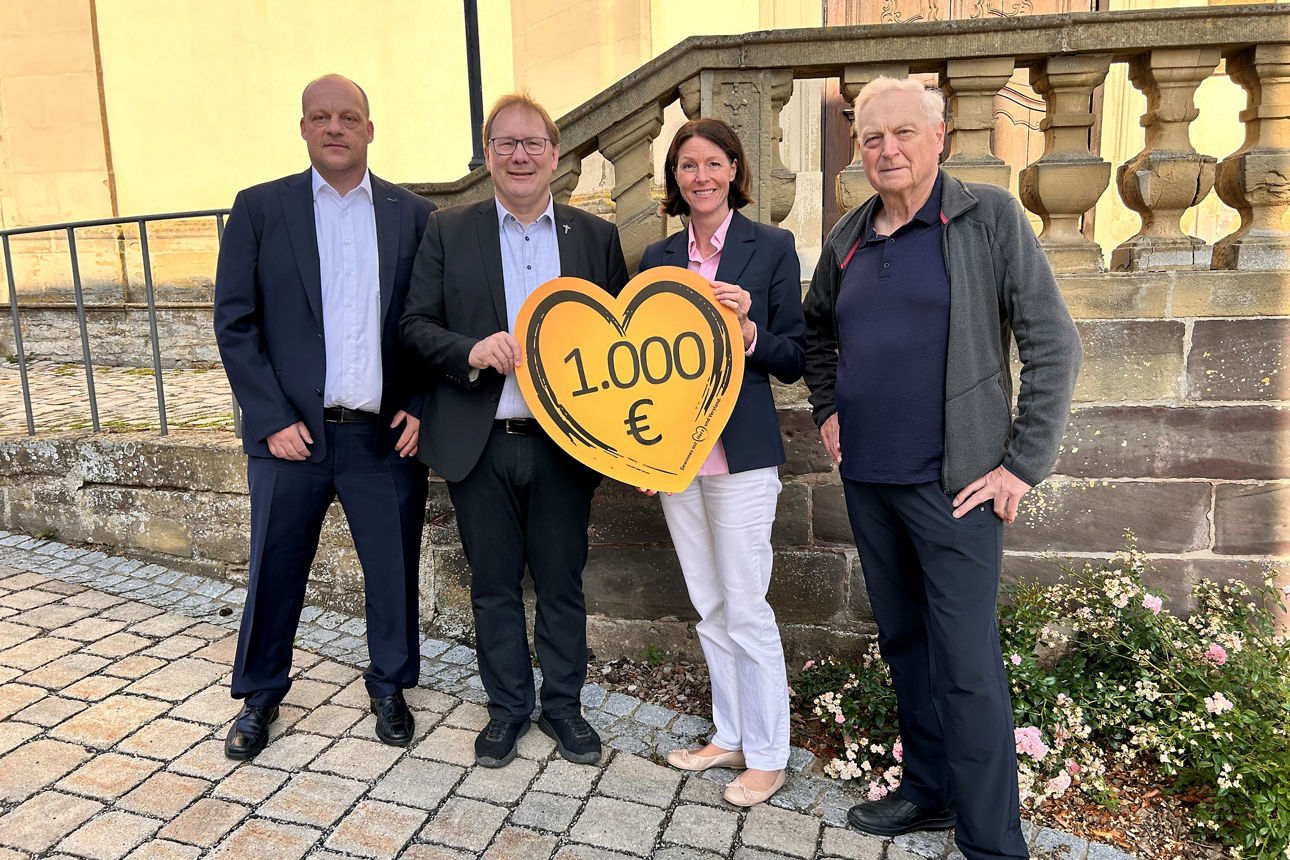 Auf dem Bild stehen die Regionalleiterin und ein Private-Banking Berater der VR-Bank mit dem Pfarrer und einem Mitglied der Kirchenverwaltung Gauaschach. Sie halten ein orangenes Herz in den Händen mit Aufschrift der Spendensumme. 