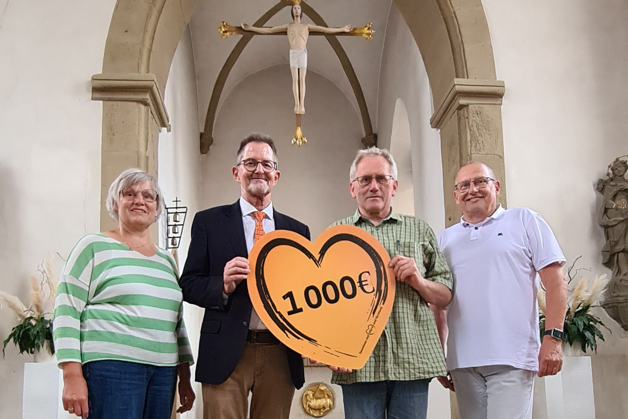 In der St. Laurentius-Kirche in Unterwaldbehrungen stehen drei Verantwortliche der Kath. Kirchenstiftung und der Spendenbotschafter der Bank. Sie halten das Spendenherz mit Aufschrift der Spendensumme in den Händen. 