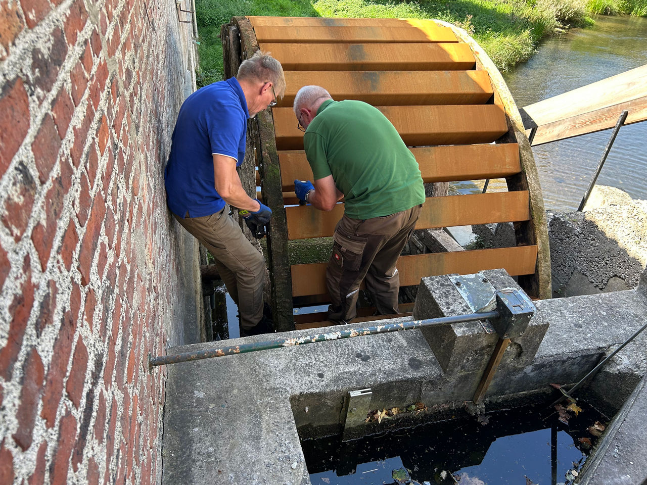 Zwei Vereinsmitglieder setzen die neuen Wasserschaufeln des Mühlrades ein.