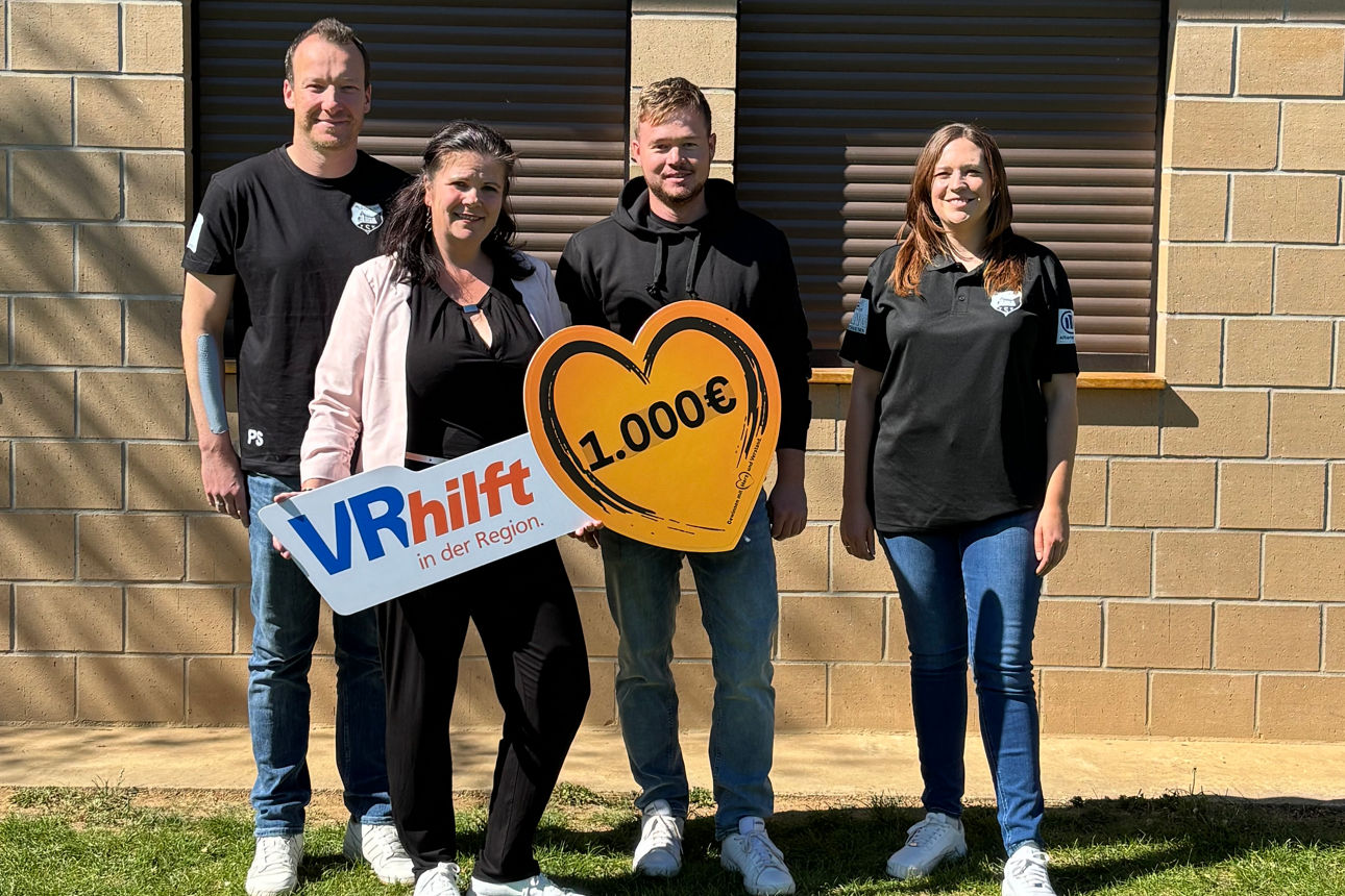 Es stehen die Vereinsverantwortlichen des TSV Waltershausen und die Filialberaterin der VR-Bank auf dem Sportgelände. Der neue Rasenmähroboter und ein Herz mit Aufschrift der Spendensumme ist zu sehen.  