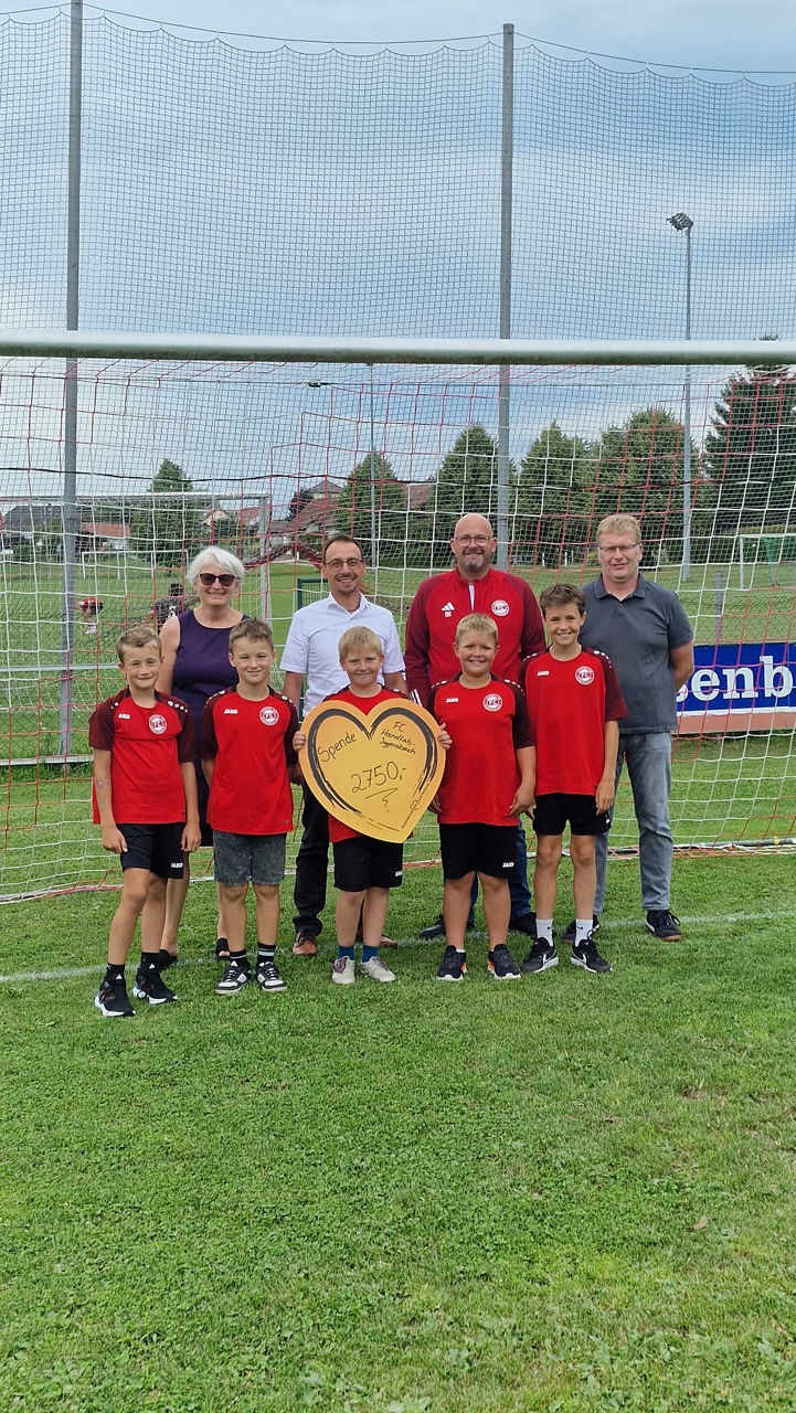 Kinder einer Jugendfußballmannschaft mit Vorstand und Kassier sowie Vertretern der Bank stehen für einem Fußballtor