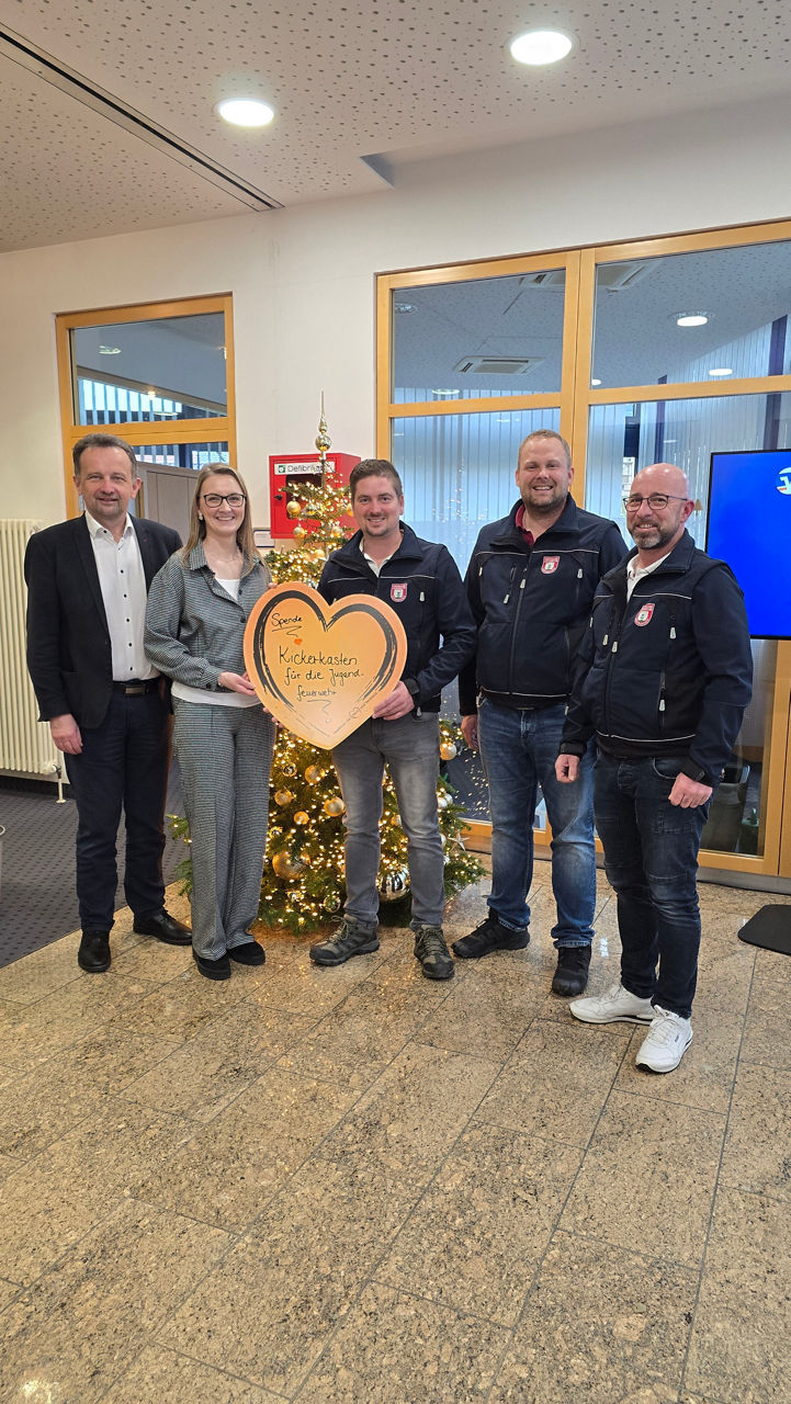 Vorstand und Marketingleitung stehen gemeinsam mit Vertretern der Feuerwehr vor einem Christbaum und halten einen Spendenscheck