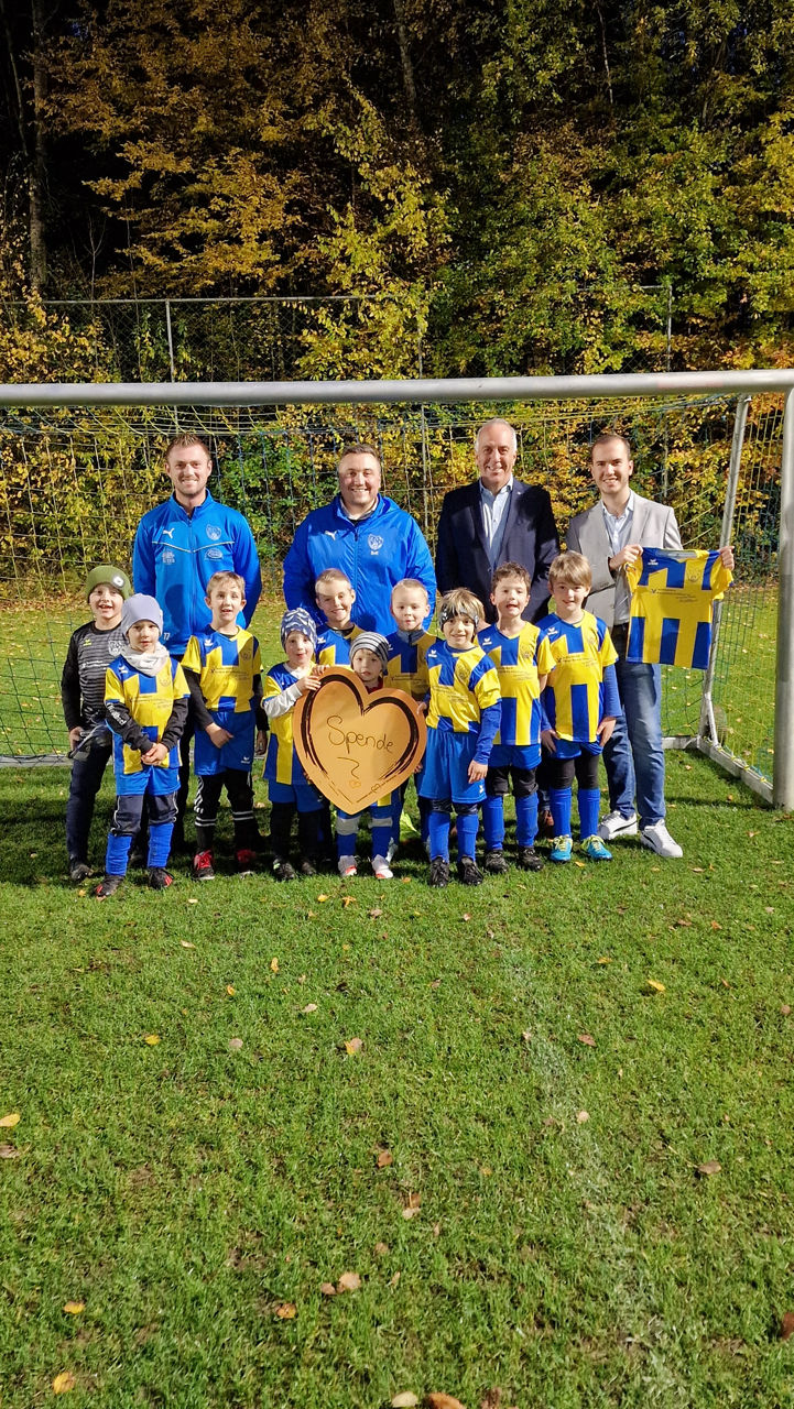 eine Fußballmannschaft aus Kindern steht mit den Trainern und Vertretern der Raiffeisenbank vor dem Fußballtor