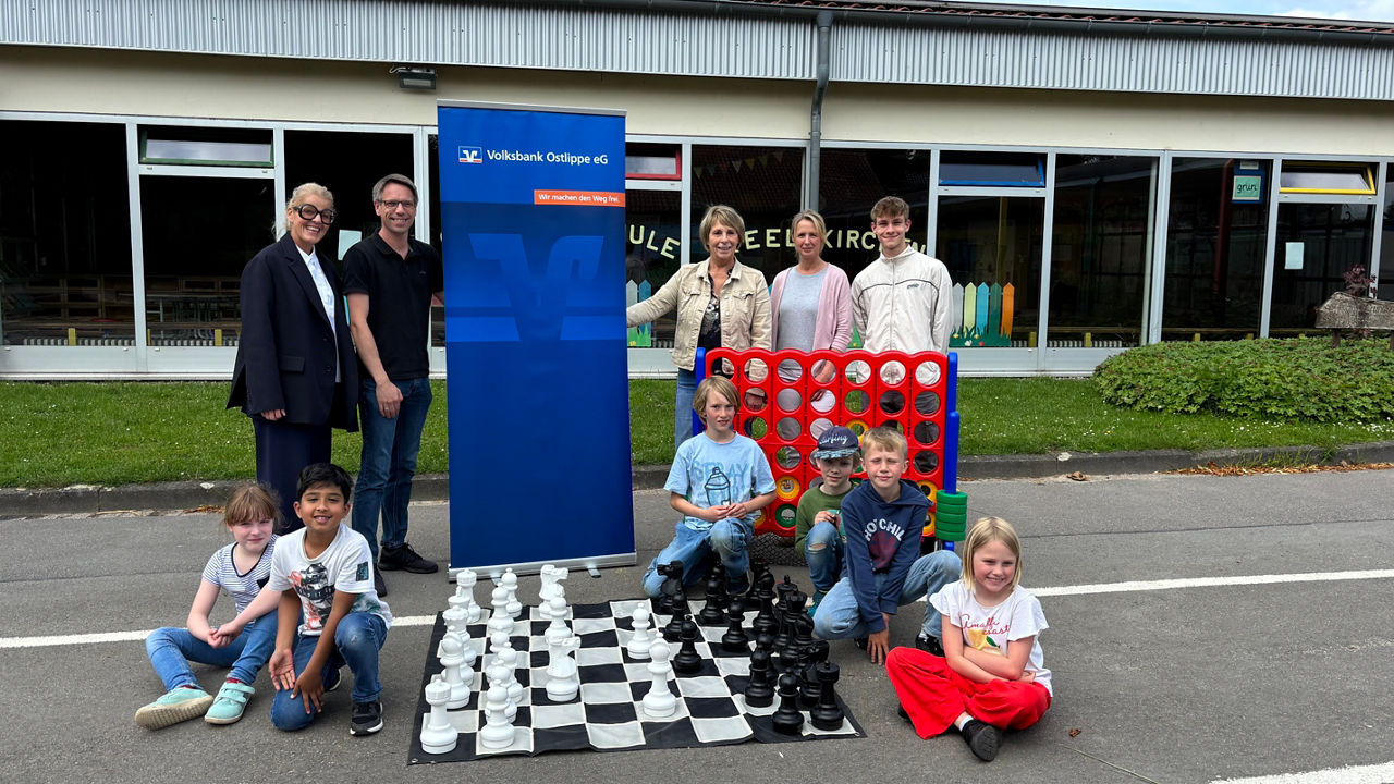 Kinder mit großen Brettspielen und fünf Erwachsenen auf dem Schulhof. 