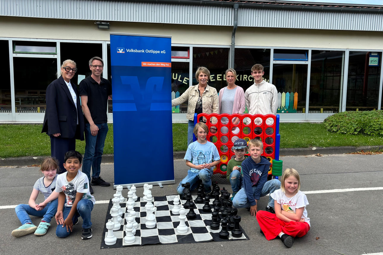 Kinder mit großen Brettspielen und fünf Erwachsenen auf dem Schulhof. 