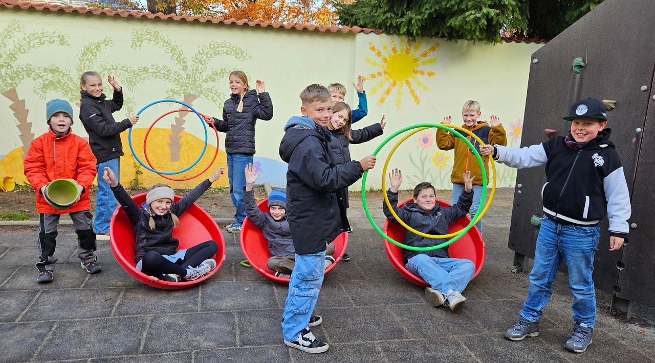 Kinder mit Spielgeräten vor ihrer gestalteten Wand