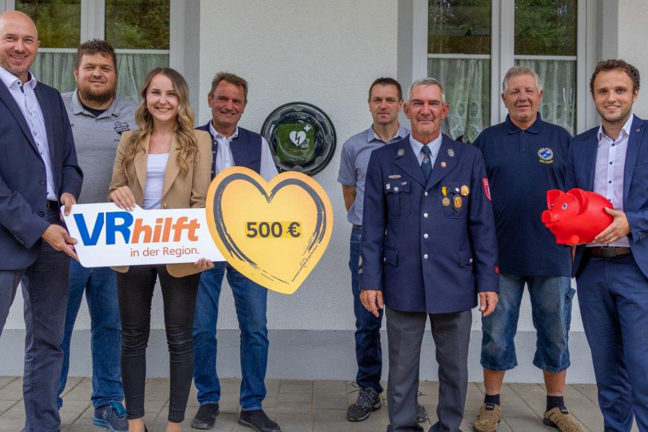 Bankmitarbeiter und eine Vertreterin einer Organisation halten einen Scheck hoch