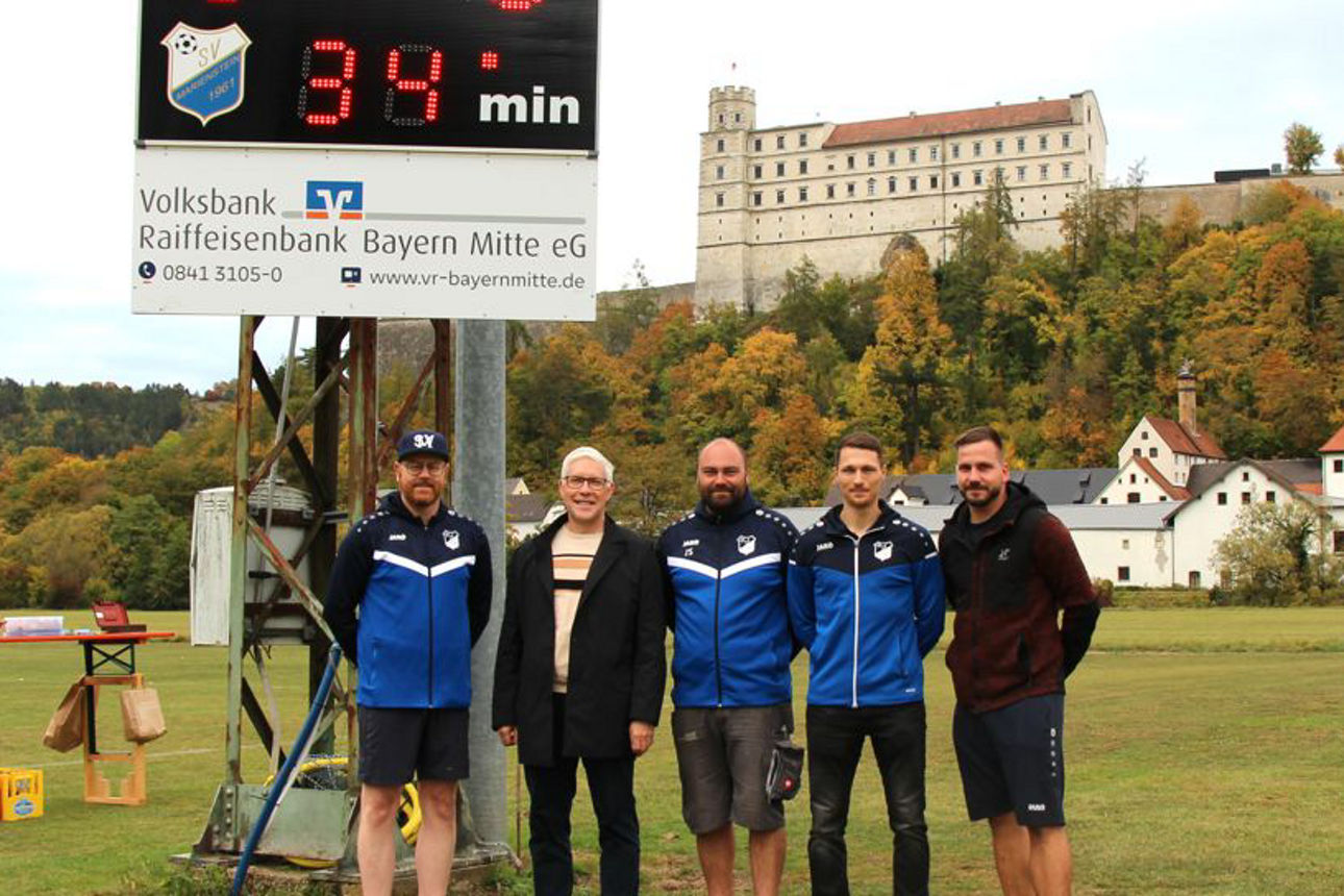 Gruppe lachender Männer vor der neuen Anzeigentafel des SV Marienstein