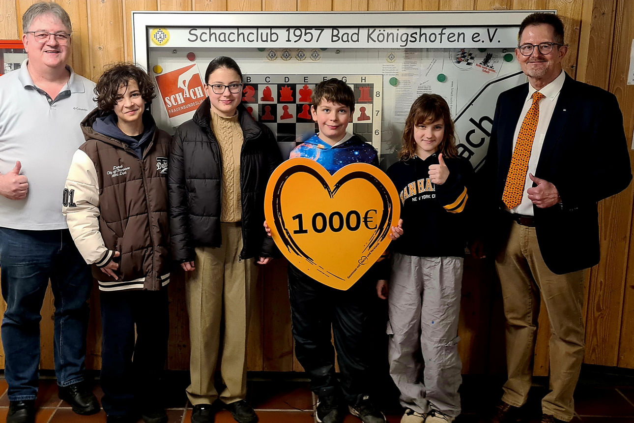 Auf dem Bild stehen der 1. Vorsitzende des Schachklubs und vier Nachwuchstalente, sowie der Spendenbotschafter der Bank. Das Kind in der Mitte hält ein Schild in Herzform mit Aufschrift der Spendensumme. 