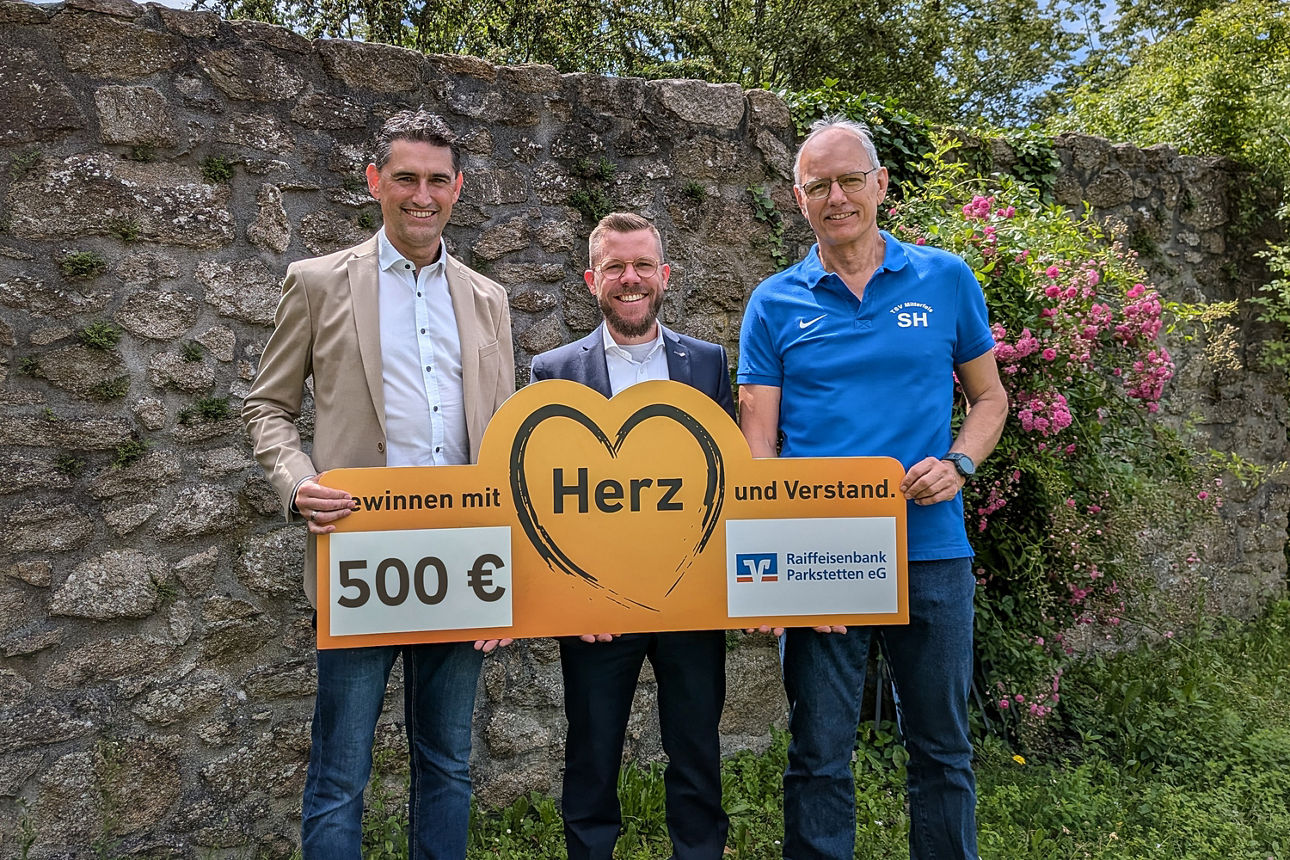 Zwei Männer überreichen einem anderen Mann einen symbolischen Scheck. 