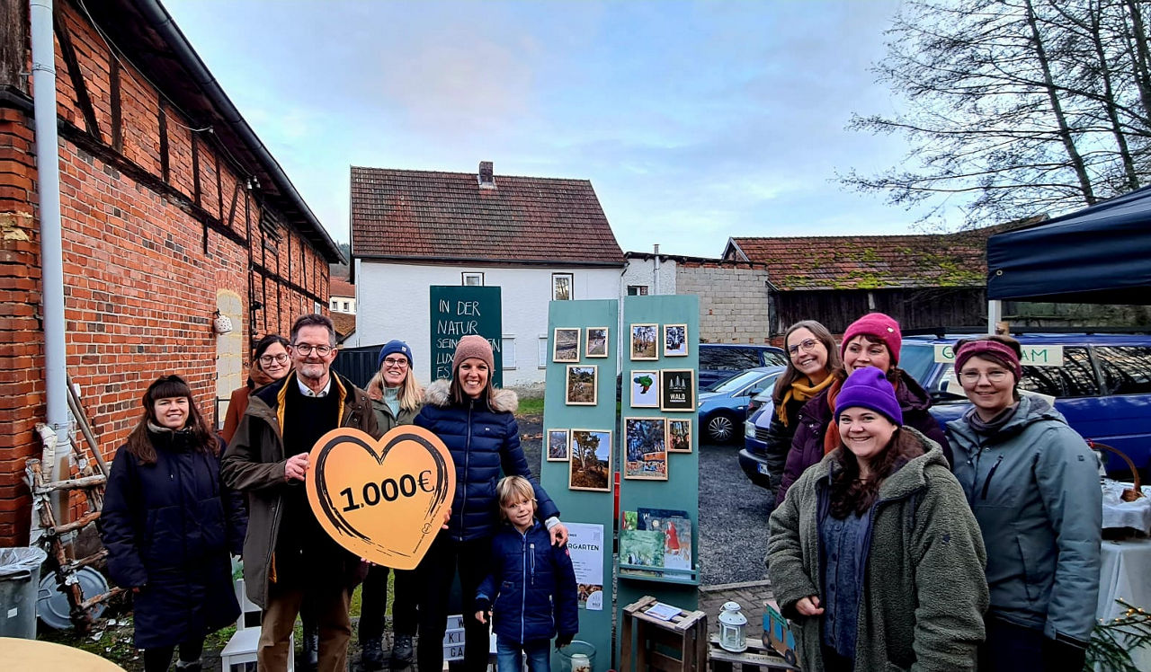 Ein Mann übergibt eine Spende von 1.000 Euro an den Verein Waldkindergarten Ostheim. Auf dem Bild sind zehn Personen zu sehen