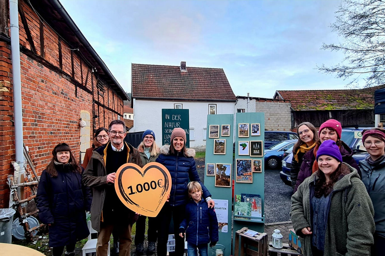 Ein Mann übergibt eine Spende von 1.000 Euro an den Verein Waldkindergarten Ostheim. Auf dem Bild sind zehn Personen zu sehen
