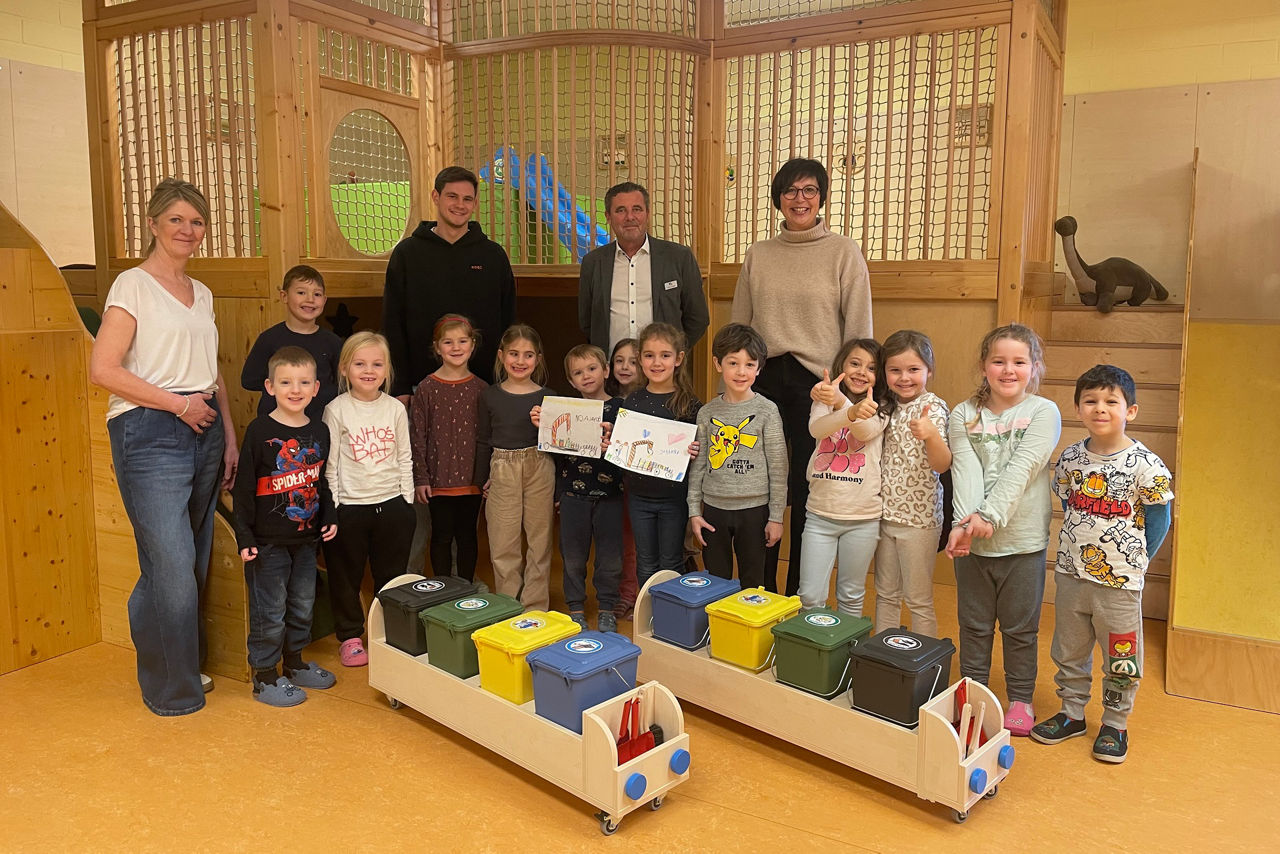 Kindergartengruppe steht vor Recycling-Behälter