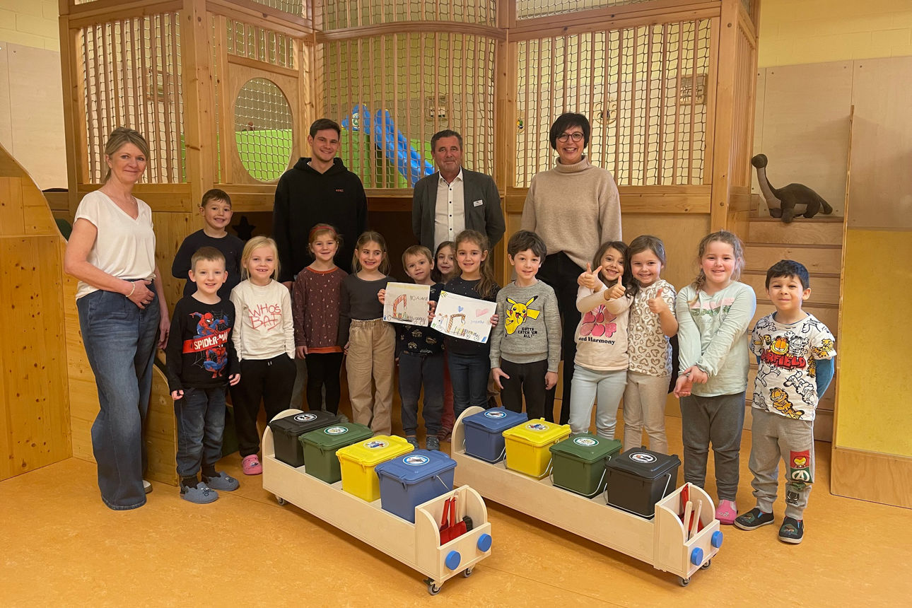 Kindergartengruppe steht vor Recycling-Behälter