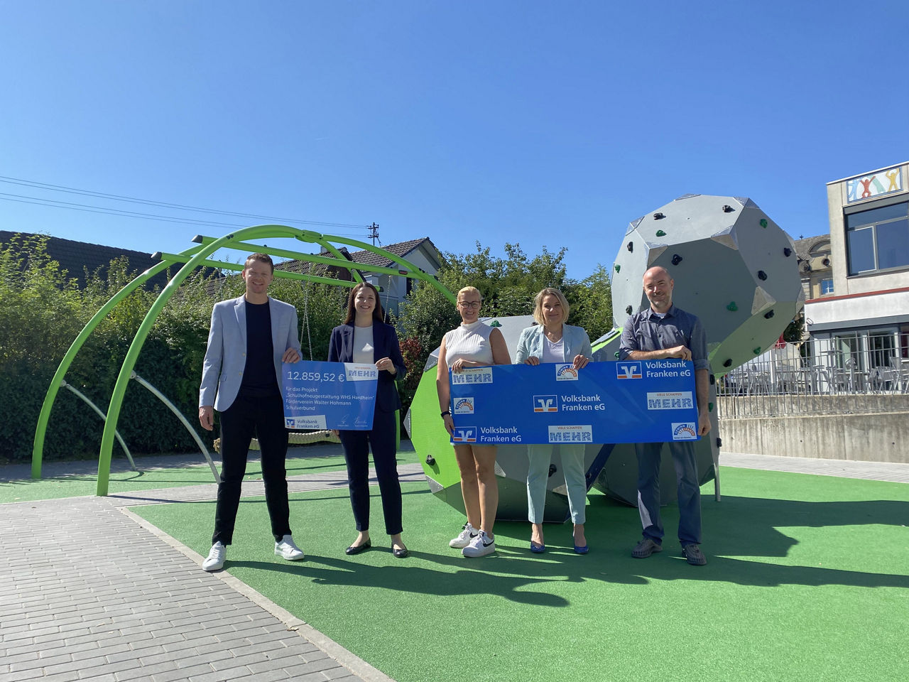 Fünf Personen halten große Spendenschecks auf dem Pausenhof in Hardheim.