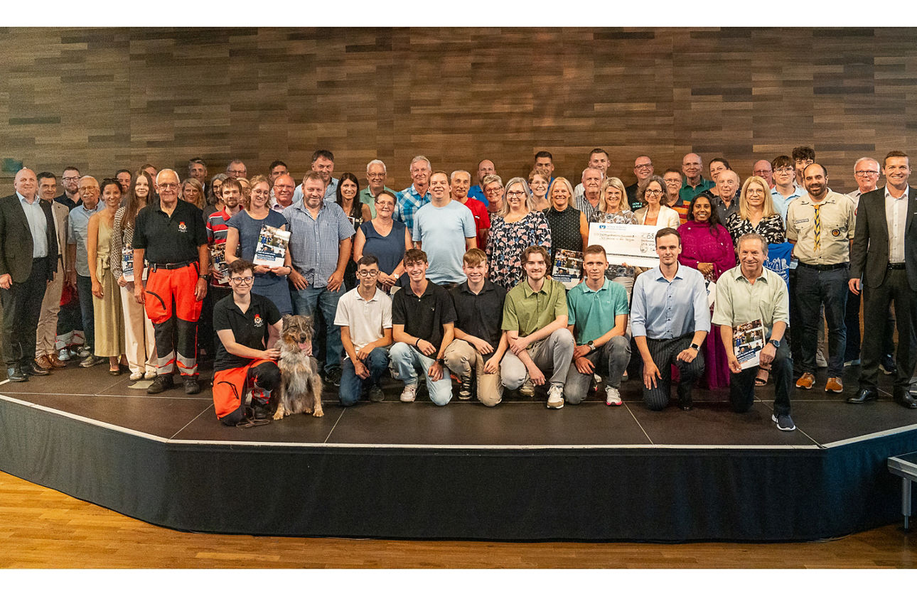 Eine große Gruppe an Menschen steht versammelt auf der Bühne und lachen in die Kamera.