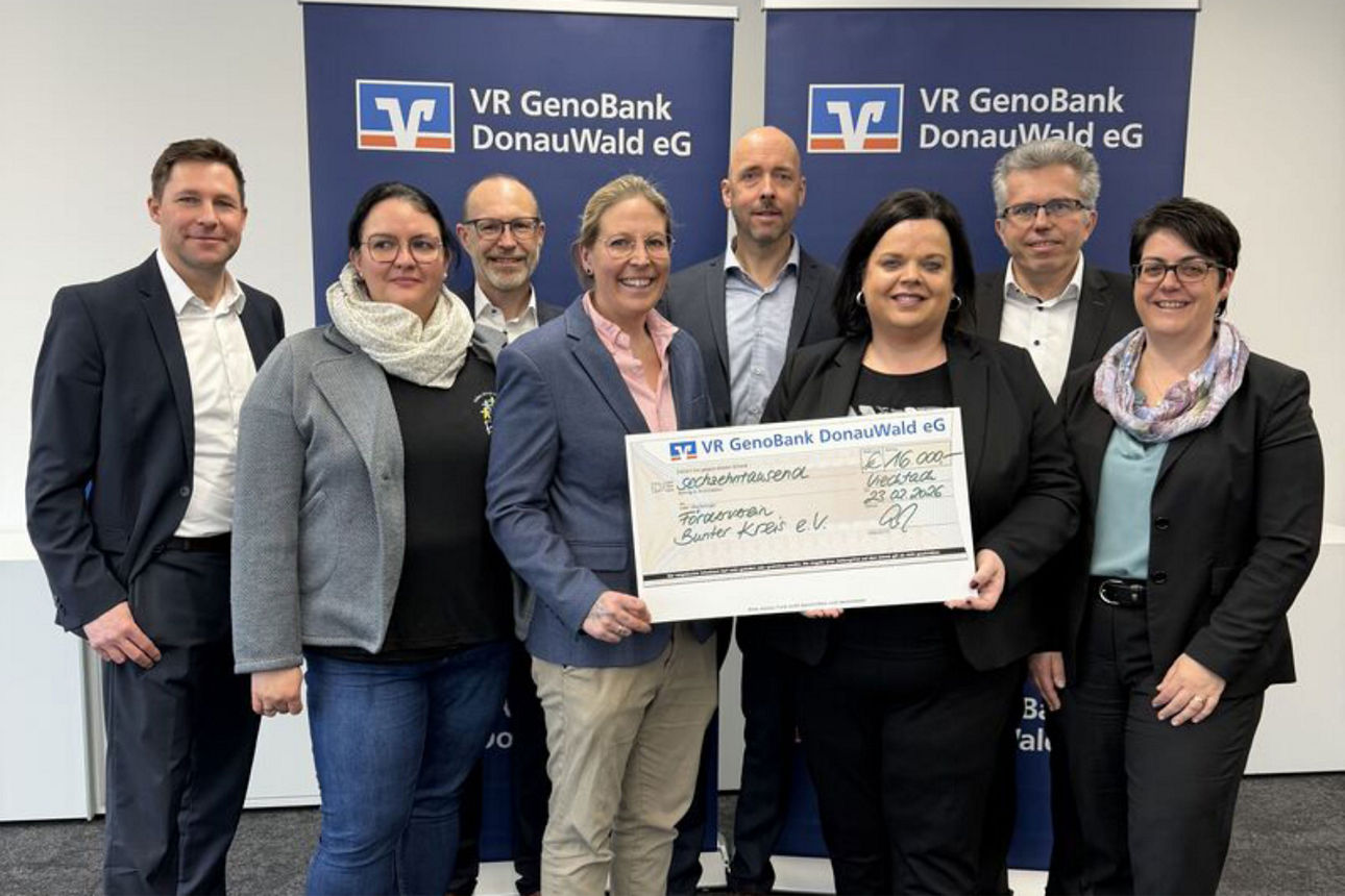 Gemini hat gesagt  Sieben Personen posieren mit einem großen Spendenscheck vor Roll-ups der VR GenoBank DonauWald eG.