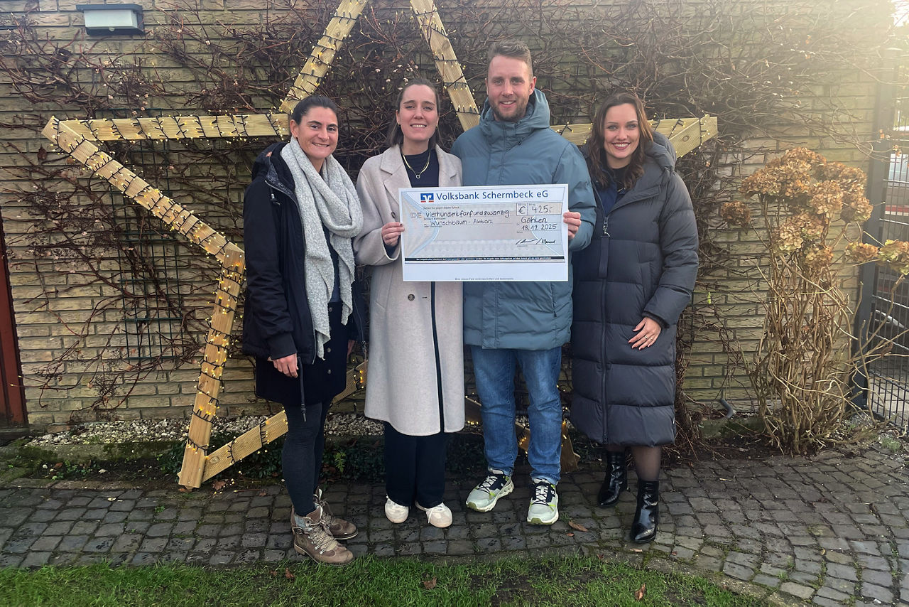 Drei Frauen und ein Mann vor einer weihnachtlichen outdoor Dekoration mit einem Scheck zu Spendenübergabe.